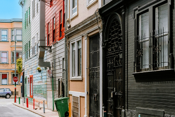 Narrow city street with colorful buildings, a stop sign, parked car, and trash bin on the sidewalk.