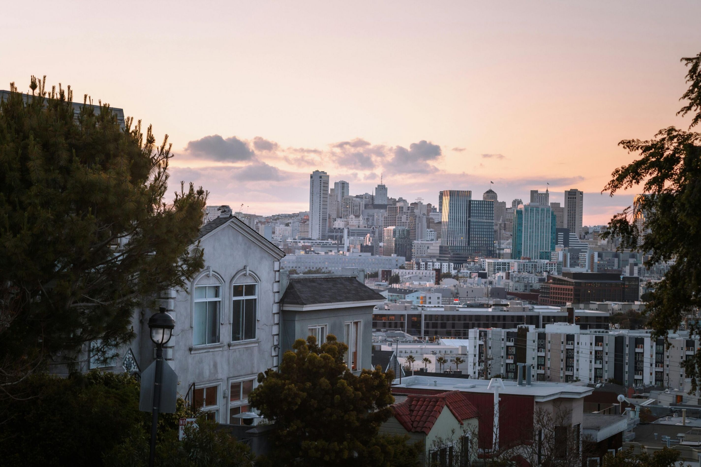 San Francisco skyline at sunset with houses and trees in the foreground.