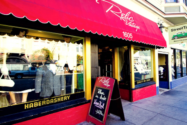 Storefront with a red awning, "Haberdashery" sign, mannequins in the window, and a sandwich board outside.