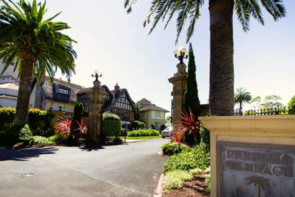 Gated entrance to a luxury estate with palm trees, ornate lamps, and a sign reading "PRESIDIO TERRACE.
