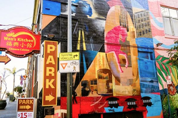 Colorful mural on a city building near Wen’s Kitchen and parking signs on a sunny street.
