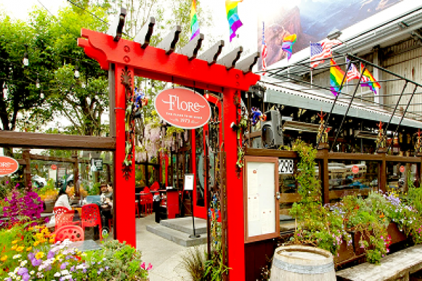 A vibrant outdoor café patio with red gate, flowers, and rainbow flags decorating the entrance.