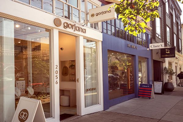 Storefronts of Gorjana and nearby shops line a sunny street with people walking on the sidewalk.