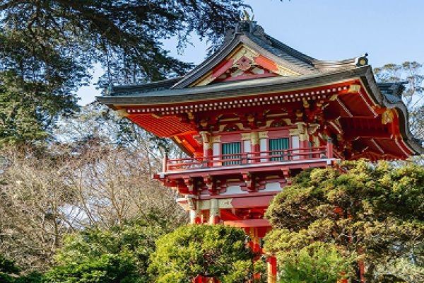 Red Japanese-style pagoda surrounded by trees and greenery, set against a clear sky background.