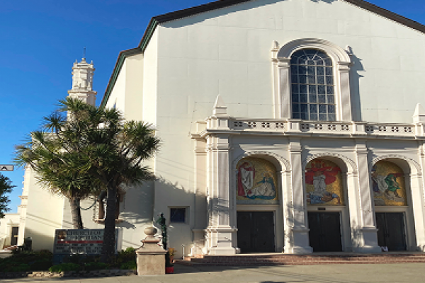 White church building with arched doors, colorful mosaics, and a street sign reading "Vienna" in front.