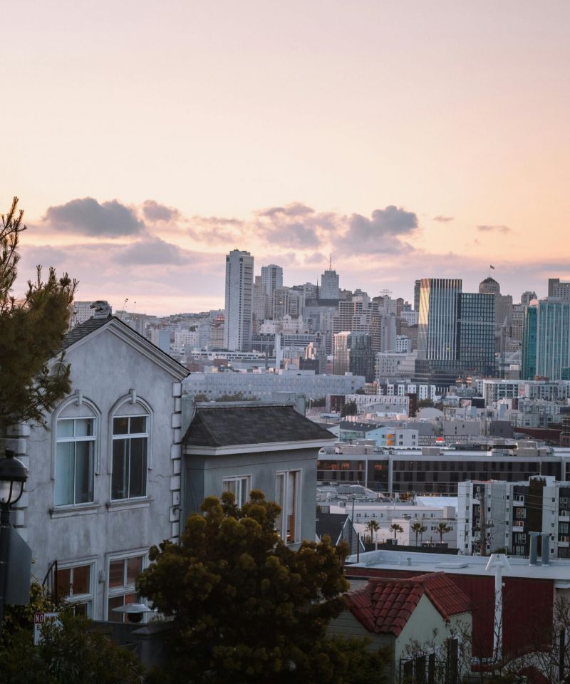 San Francisco skyline at sunset with houses and trees in the foreground.