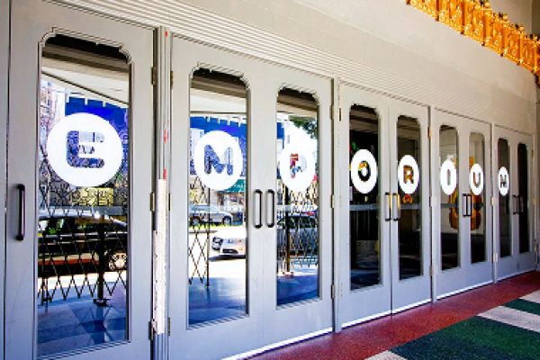 Row of glass doors with "EMPORIUM" spelled out in circular letters, reflecting street and cars outside.