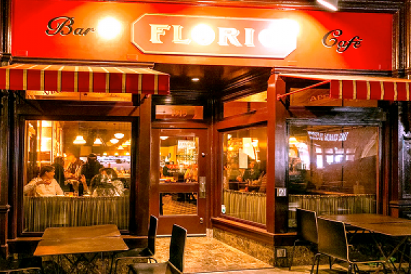 A warmly lit café with red-striped awnings and people dining inside at night.