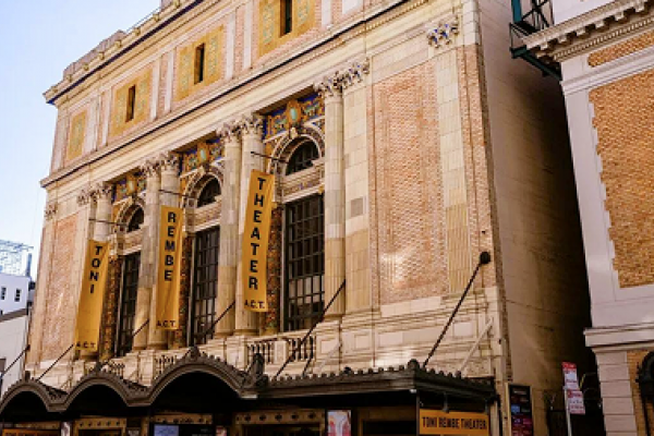 Historic theater with banners reading "Toni Rembe Theater" on a brick facade, under a clear sky.