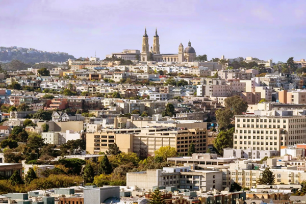 View of a cityscape with clustered buildings and a large church on a hill in the background under a clear sky.