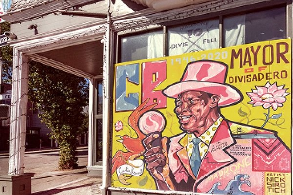 Colorful mural of a man in a hat with “Mayor of Divisadero” painted on a building corner in a city.