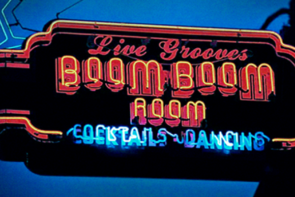Neon sign reading "Live Grooves Boom Boom Room Cocktails Dancing" glowing against a dark background.