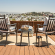 Two patio chairs and a table on a deck overlooking a cityscape under a clear blue sky.