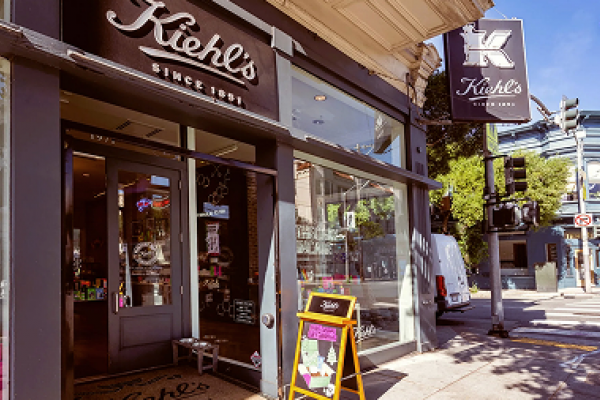 Street view of a Kiehl’s store entrance with signs, window displays, and a sidewalk chalkboard.