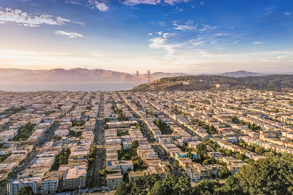 Aerial view of San Francisco neighborhoods with the Golden Gate Bridge and hills in the background at sunset.
