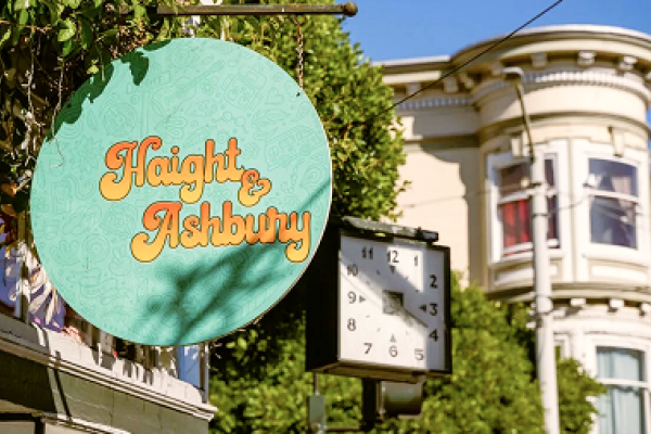 Round "Haight & Ashbury" sign with clock and Victorian building in sunny urban setting.