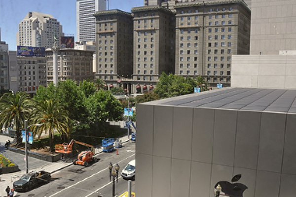 View of a city street with trees, tall buildings, and an Apple store in the foreground.